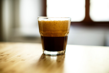 A glass of iced espresso lying on a wooden table corner