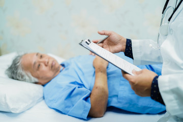 Doctor talking about diagnosis and note on clipboard with Asian senior or elderly old lady woman while lying on bed in nursing hospital ward : healthy strong medical concept.