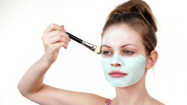 Young woman applying with brush green white mud mask to her face. Teen girl taking care of oily skin, purifying the pores. Beauty treatment. Skincare.