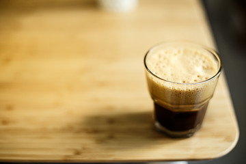 A glass of iced espresso lying on a wooden table corner