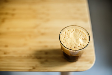 A glass of iced espresso lying on a wooden table corner