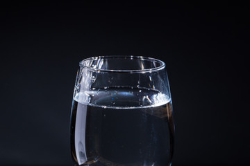 Glass of water on a gray background with drops in different directions