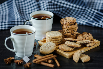 Two cups of tea and various cookies on dark wooden background