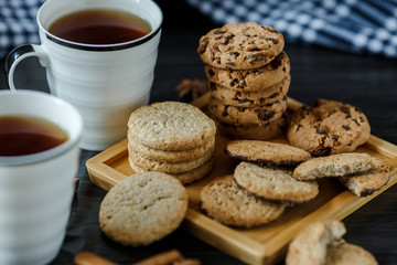 Two cups of tea and various cookies on dark wooden background