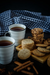 Two cups of tea and various cookies on dark wooden background