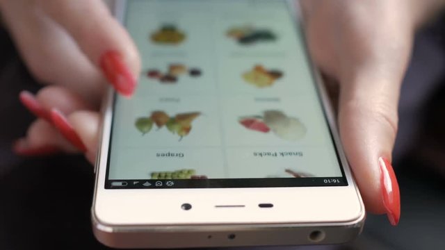 Young Woman With Manicure Orders Food Home In An Online Store Using A Smartphone. Female Selects The Tropic Fruit  In The Grocery Online Store. Close Up. 4K UHD. LOS ANGELES - October 2018.