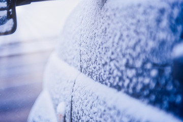 Rear view mirror on a snow-covered car, standing in the Parking lot near the house on a cold morning, the sun shines into the camera. Closeup of car tires in winter on the road covered with snow.