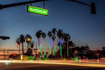 Traffic lights and streaking vehicles cross intersection as sun sets behind holiday lights on...