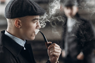 stylish man in retro outfit, smoking wooden pipe. sherlock holmes look cosplay.  england in 1920s...