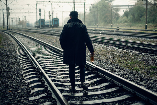 Silhouette Of Stylish Gangster Man With Bottle Whiskey Walking On Railway Road. England In 1920s Theme. Fashionable Brutal Confident Man. Atmospheric Moments