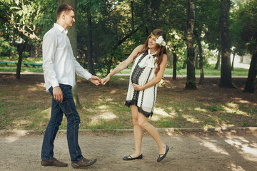 Happy fun couple, pregnant woman and handsome man dancing in sunny park, in fashionable vintage clothes