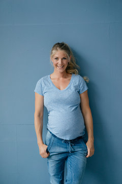 Portrait of smiling pregnant woman standing at blue wall