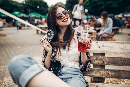 stylish hipster woman in sunglasses with red lips holding lemonade and old photo camera. boho girl holding cocktail and smiling at street food festival. summertime. summer  vacation