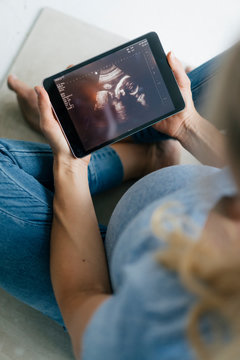 Pregnant woman sitting on the floor looking at ultrasound picture on tablet
