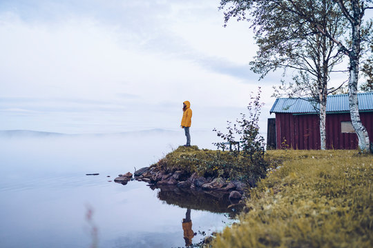 Sweden, Lapland, man wearing windbreaker standing at water's edge looking at distance