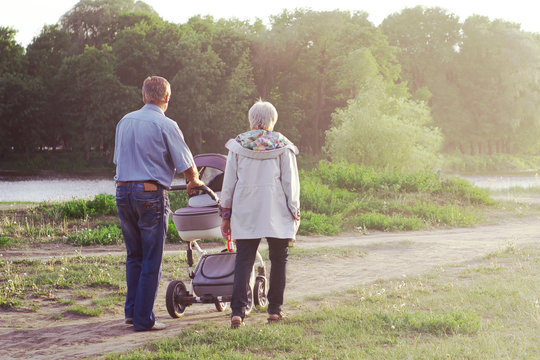 Grandparents are walking with a baby in a stroller in a park by the river