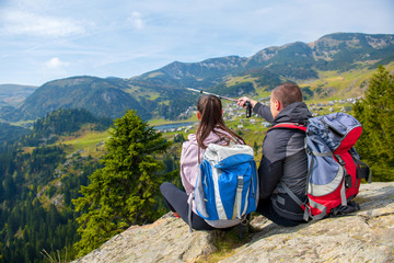 Fototapeta premium Two hikers at viewpoint in the mountains enjoying beautiful view of the valley with a lake.