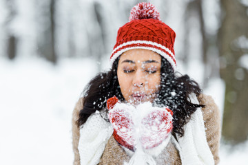 attractive african american woman blowing snow in park in winter forest