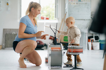 Happy pregnant mother with toddler son playing toy drums