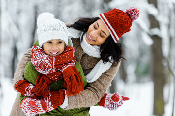 attractive african american mother hugging cute daughter in winter forest