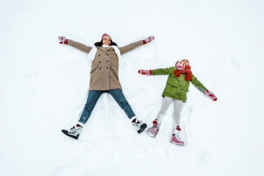 attractive african american mother and cute daughter doing snow angels in winter forest