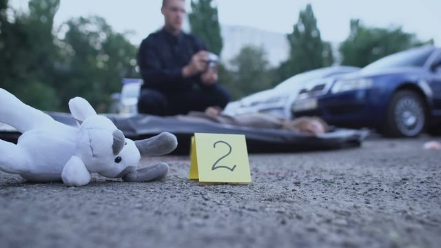 Forensic expert marking evidence, policeman making photo of victim, toy on road