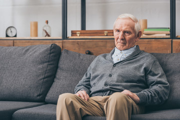 upset retired man with grey hair sitting on sofa