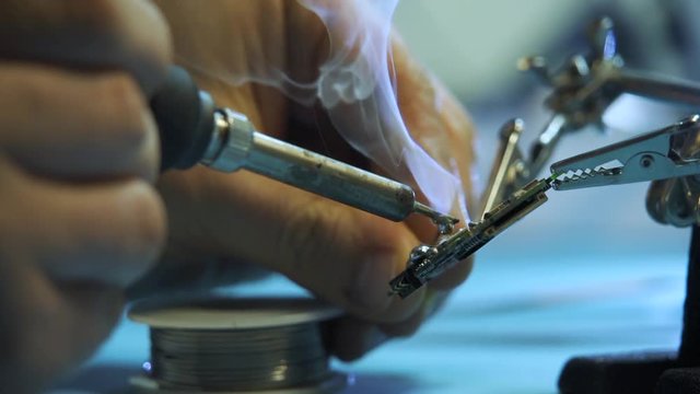 The engineer solders the chip with a soldering iron. Smoke rises. Slow motion