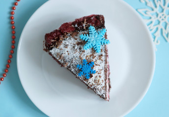 Chocolate cake slice with snowflakes decoration and cherry on winter background top view.