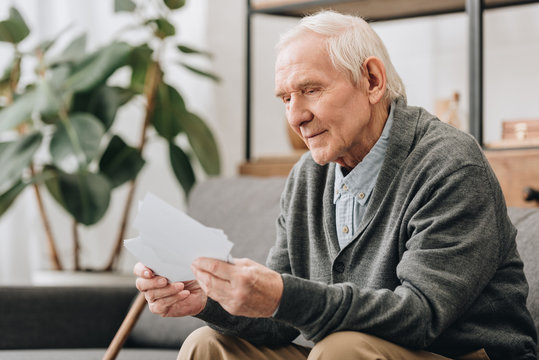 happy pensioner with grey hair looking at photos in living room