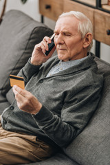 senior man talking on smartphone and looking at credit card