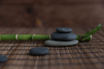 Obraz na płótnie Canvas Pyramids of gray zen pebble meditation stones with green bamboo leaves and on wooden background. Concept of harmony, balance and meditation, spa, massage, relax