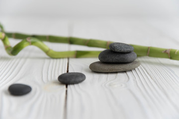 Fototapeta na wymiar Pyramids of gray zen pebble meditation stones with green bamboo leaves and on wooden background. Concept of harmony, balance and meditation, spa, massage, relax