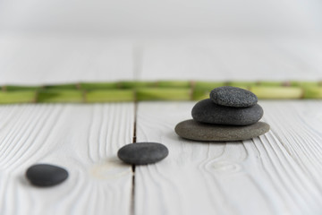Pyramids of gray zen pebble meditation stones with green bamboo leaves and on wooden background. Concept of harmony, balance and meditation, spa, massage, relax
