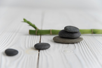 Obraz na płótnie Canvas Pyramids of gray zen pebble meditation stones with green bamboo leaves and on wooden background. Concept of harmony, balance and meditation, spa, massage, relax
