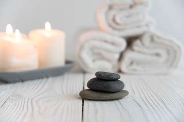 Fototapeta na wymiar Beautiful spa still life. Twisted towel, aromatic candles and black hot stone on wooden background. Hot stone therapy. Concept of harmony, balance and meditation, relax, massage, beauty spa treatment.