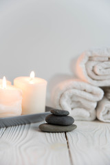 Fototapeta na wymiar Beautiful spa still life. Twisted towel, aromatic candles and black hot stone on wooden background. Hot stone therapy. Concept of harmony, balance and meditation, relax, massage, beauty spa treatment.