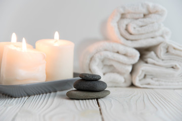 Beautiful spa still life. Twisted towel, aromatic candles and black hot stone on wooden background. Hot stone therapy. Concept of harmony, balance and meditation, relax, massage, beauty spa treatment.