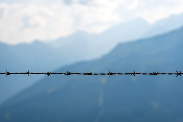 Barbed wire in close-up. The background is a mountain landscape.