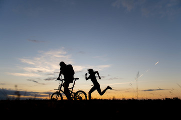 Fototapeta na wymiar people riding bike and running in meadow with sunset background