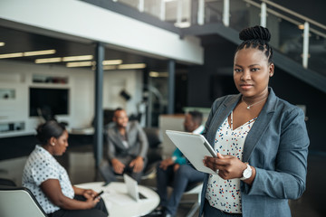 Portrait of a confident black businesswoman using her tablet looking into the camera with all african american team in the background