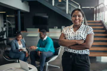 Portrait of a confident black businesswoman smiling with her arms crossed and all african team in the background