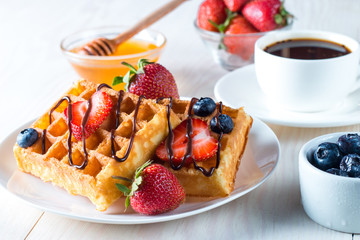 Fresh homemade food of berry Belgian waffles with honey, chocolate, strawberry, blueberry, maple syrup and cream. Healthy dessert breakfast concept with juice