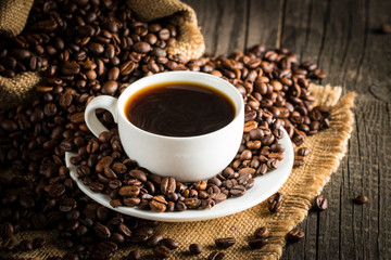 Fototapeta premium Coffee cup and beans on a rustic background. Coffee Espresso and a piece of cake with a curl. Cup of Coffee and coffee beans on table.
