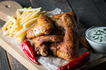 Barbecue grilled chicken wings close up with fries, tomato ketchup sauce and beer on wooden background. Meat food concept. 