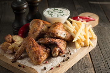 Barbecue grilled chicken wings close up with fries, tomato ketchup sauce and beer on wooden background. Meat food concept. 