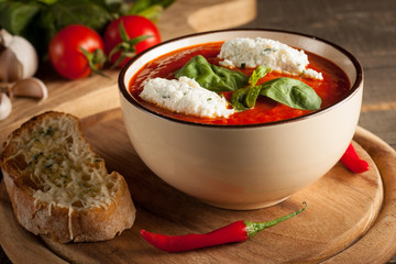 Fresh, healthy tomato soup with basil, pepper, garlic, tomatoes and bread on wooden background. Spanish gazpacho soup.