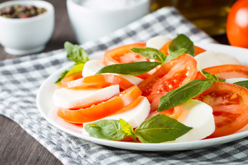 Photo of Caprese Salad with tomatoes, basil, mozzarella, olives and olive oil on wooden background. Italian traditional caprese salad ingredients. Mediterranean, organic and natural food concept.