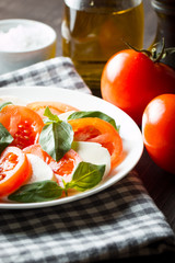 Photo of Caprese Salad with tomatoes, basil, mozzarella, olives and olive oil on wooden background. Italian traditional caprese salad ingredients. Mediterranean, organic and natural food concept.