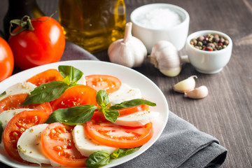 Photo of Caprese Salad with tomatoes, basil, mozzarella, olives and olive oil on wooden background. Italian traditional caprese salad ingredients. Mediterranean, organic and natural food concept.